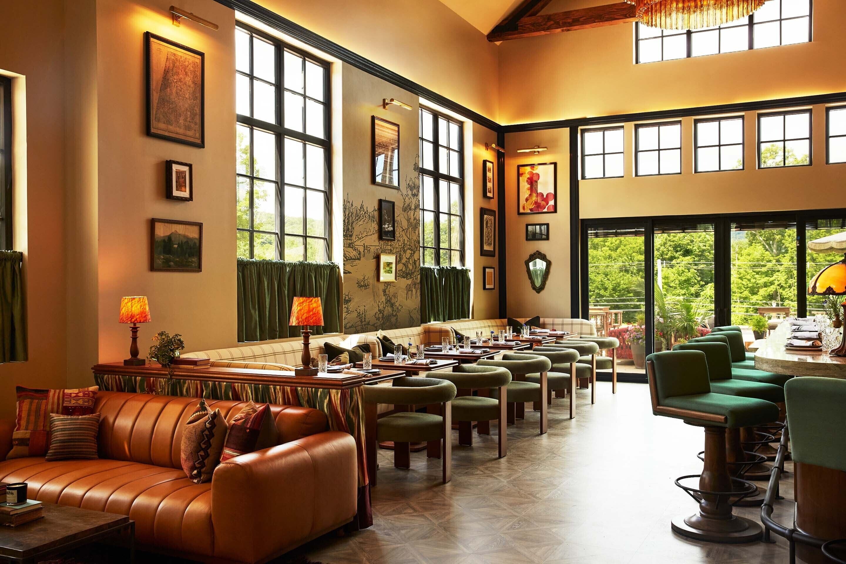 A spacious hotel lobby with leather sofas, green chairs, and a dining area with tables and chairs.