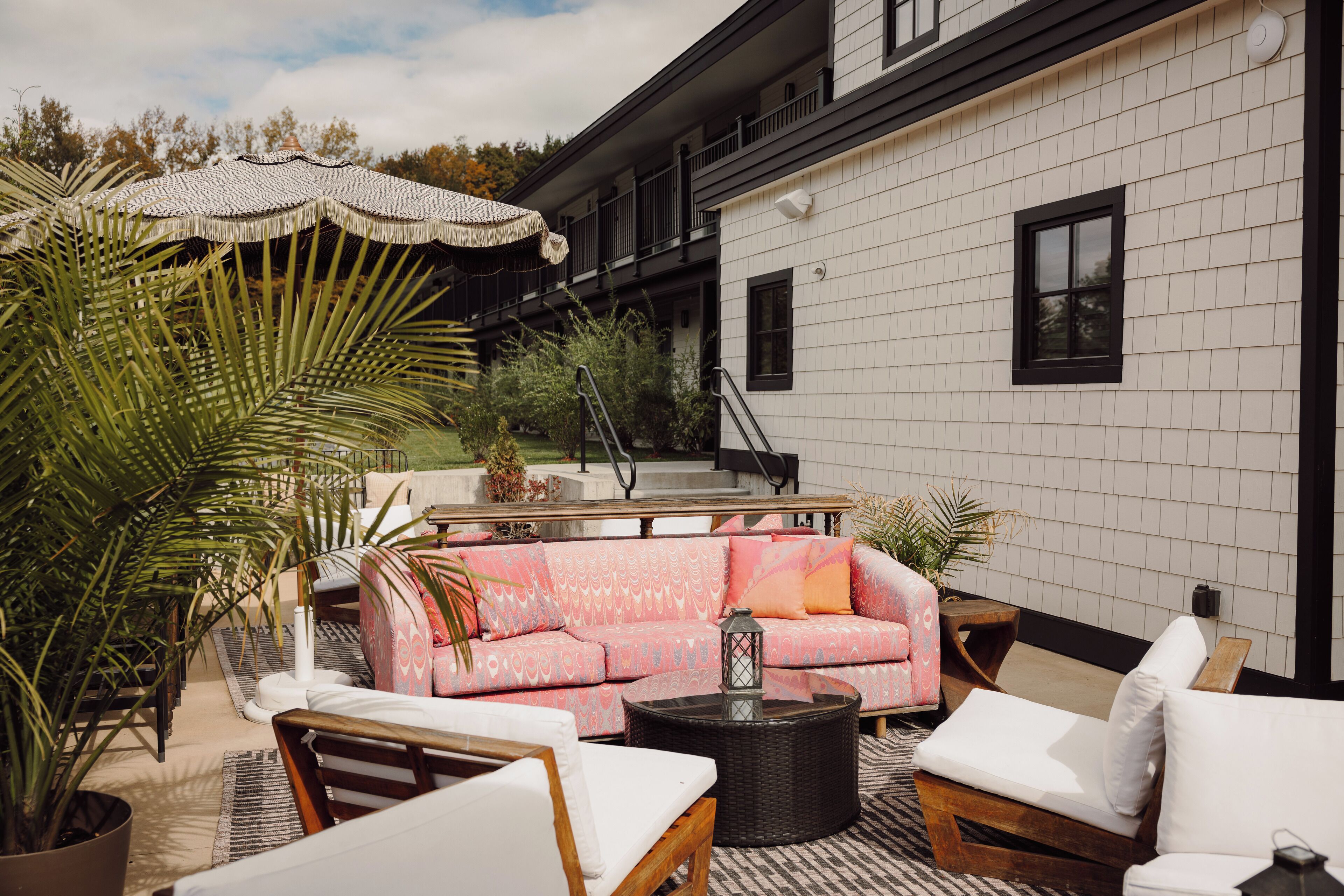 Ein Sitzbereich im Freien mit einer rosa Couch, weißen Lounge-Stühlen und einem runden Tisch.