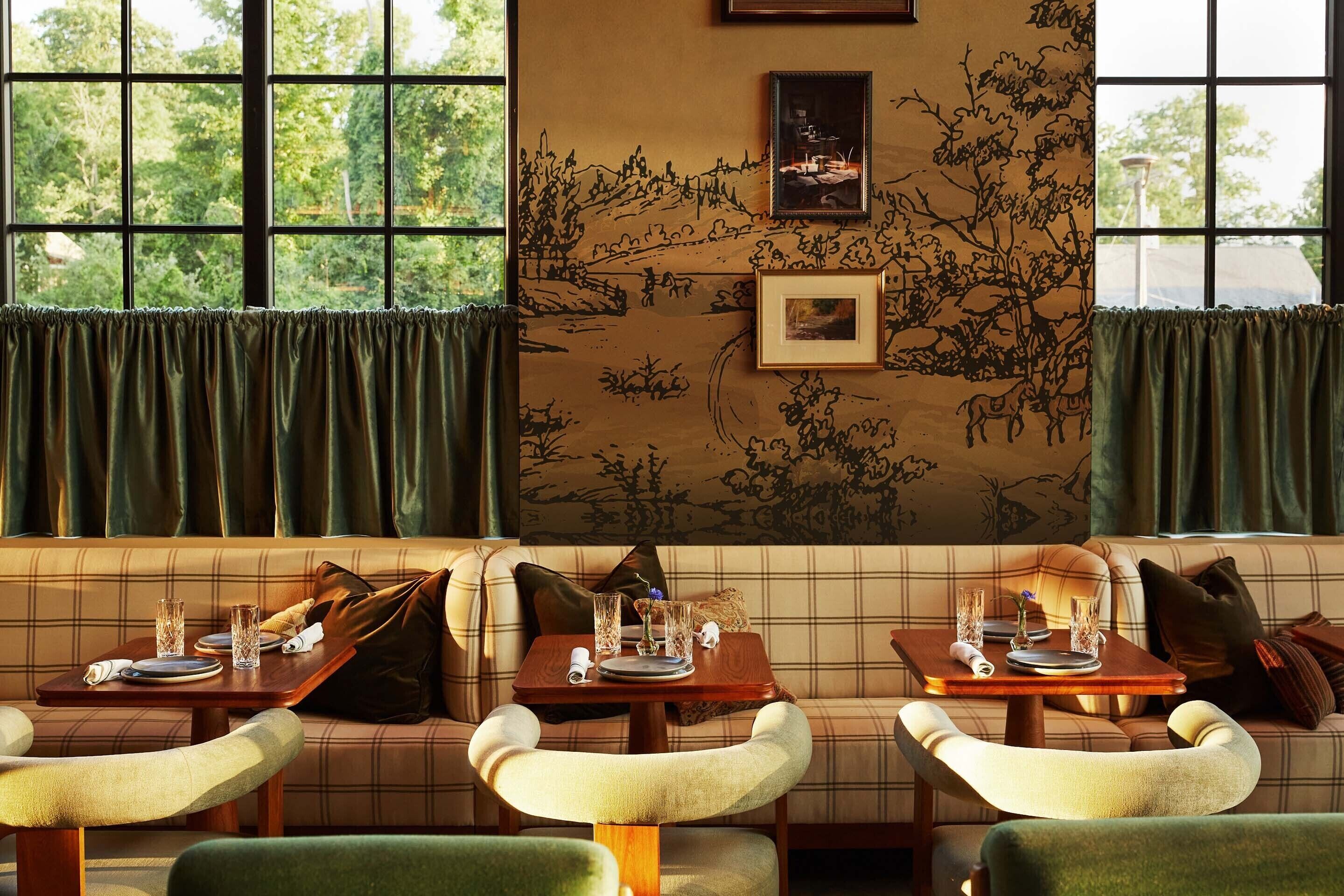 Un comedor acogedor con un sofá de cuadros, dos mesas de comedor dispuestas con platos, vasos y cubiertos, y un mural en la pared.