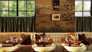 A cozy dining area with a plaid sofa, two dining tables set with plates, glasses, and cutlery, and a mural on the wall.