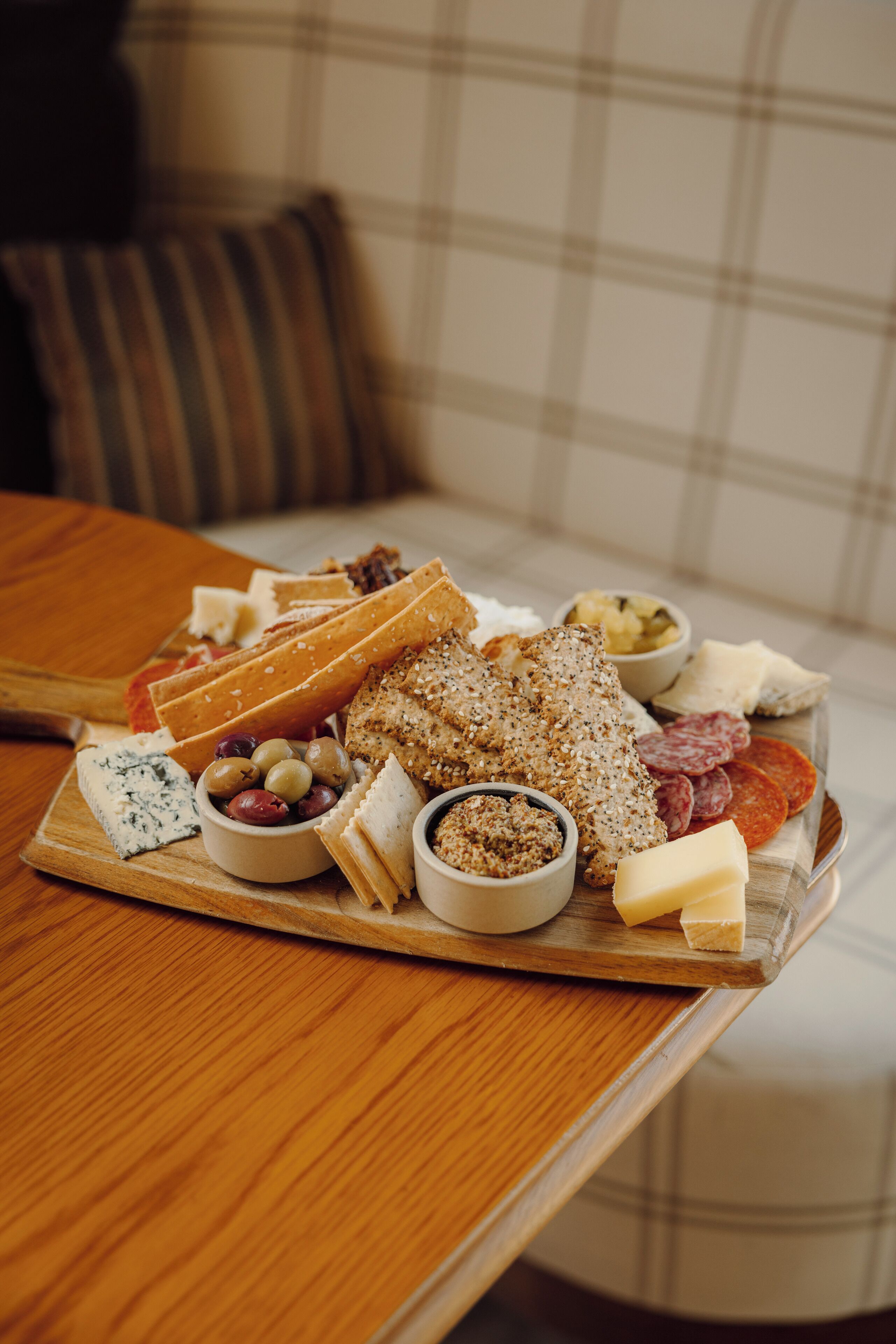 A wooden board with various cheeses, olives, and meats on a table.