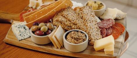 A wooden board with various cheeses, olives, and meats on a table.