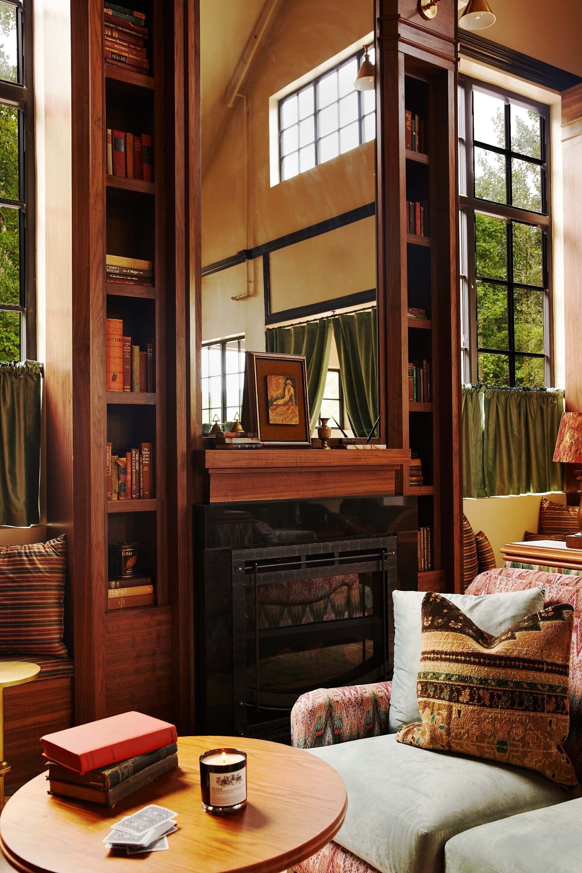 A cozy room with a fireplace, a bookshelf, a comfortable seating area, and large windows.