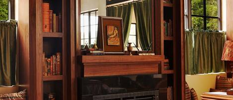 A cozy room with a fireplace, a bookshelf, a comfortable seating area, and large windows.