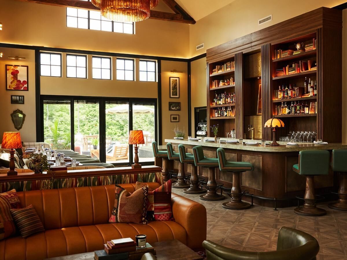 En rummelig lounge med lædersofa, barområde med barstole og store vinduer med udsigt over grønne områder.