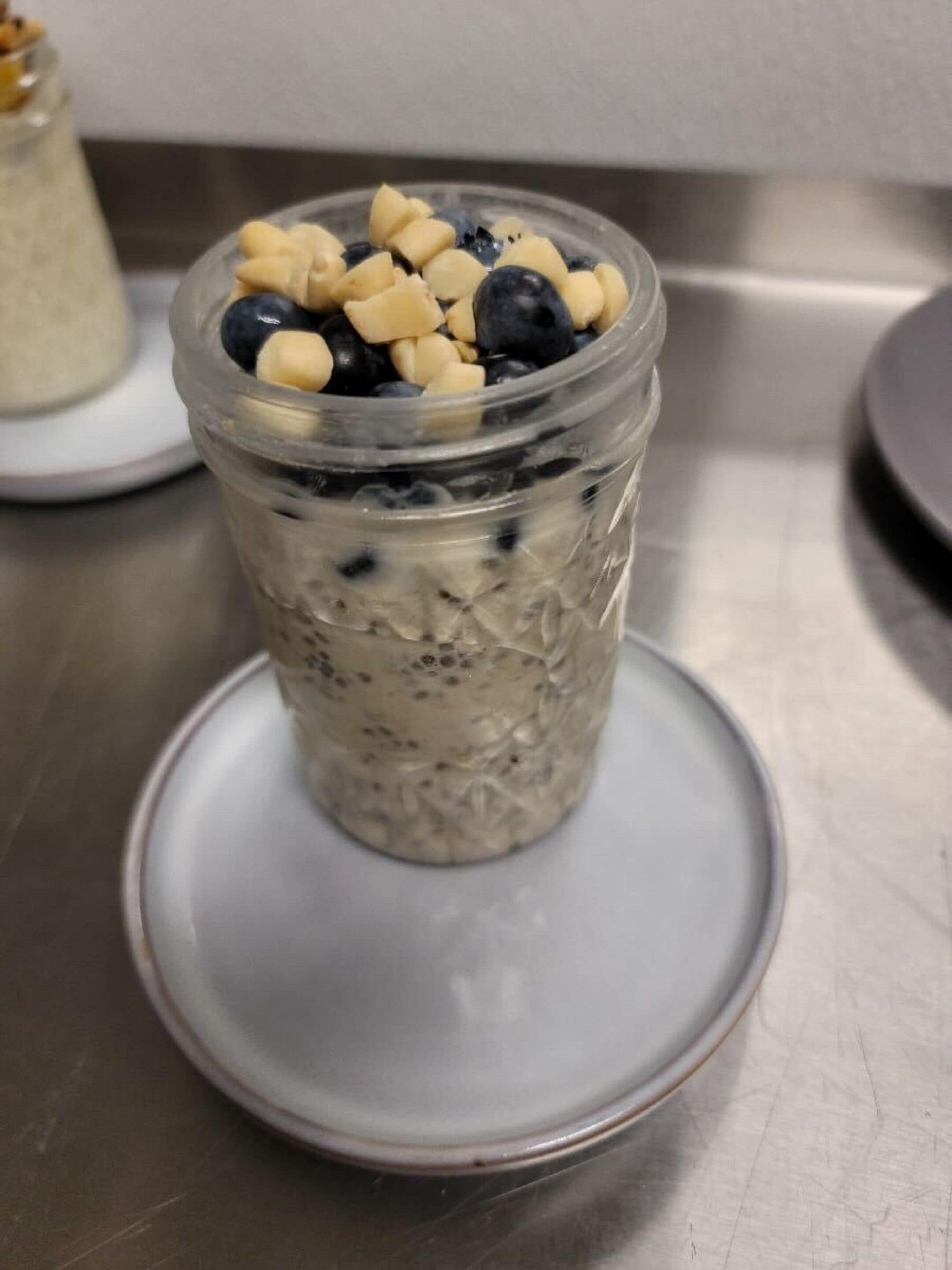 Un frasco de vidrio transparente con avena y arándanos sobre un plato blanco.