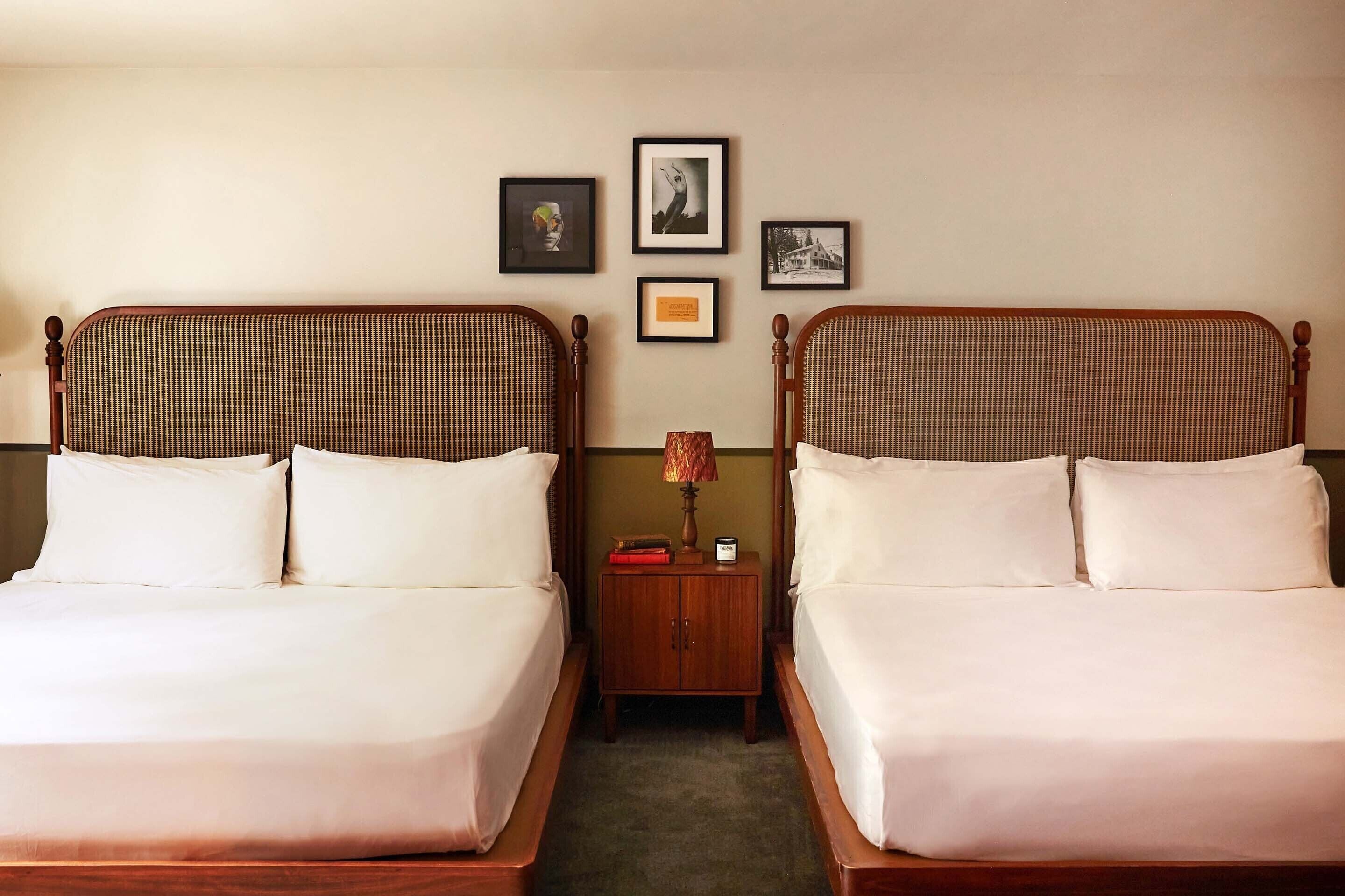 A hotel room with two beds, a nightstand, and framed pictures on the wall.