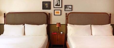 A hotel room with two beds, a nightstand, and framed pictures on the wall.