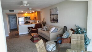 A living room with a sofa, chairs, a coffee table, and a dining area with a kitchen. - Gorgeous beachfront studio penthouse! (Clearwater Beach)