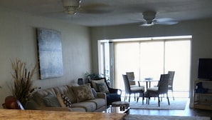 A spacious kitchen with a large island, wooden bar stools, and a dining area with chairs and a table. - Gorgeous beachfront studio penthouse! (Clearwater Beach)