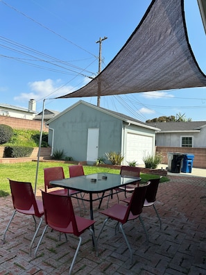 Une terrasse avec une table et des chaises, un espace ombragé et un bâtiment en arrière-plan.