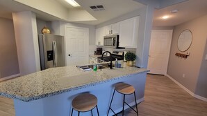 Una cocina moderna con encimera de granito, electrodomésticos de acero inoxidable y una pequeña isla con taburetes de bar.