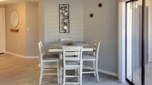Un comedor con una mesa y sillas, un adorno en la pared y un ventanal corredero que da a un balcón.