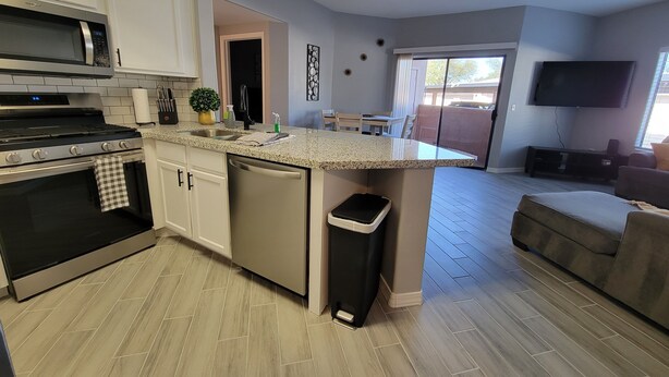 Una cocina moderna con una isla central, un comedor con mesa y sillas, una sala de estar con sofá y televisor, y un ventilador de techo.