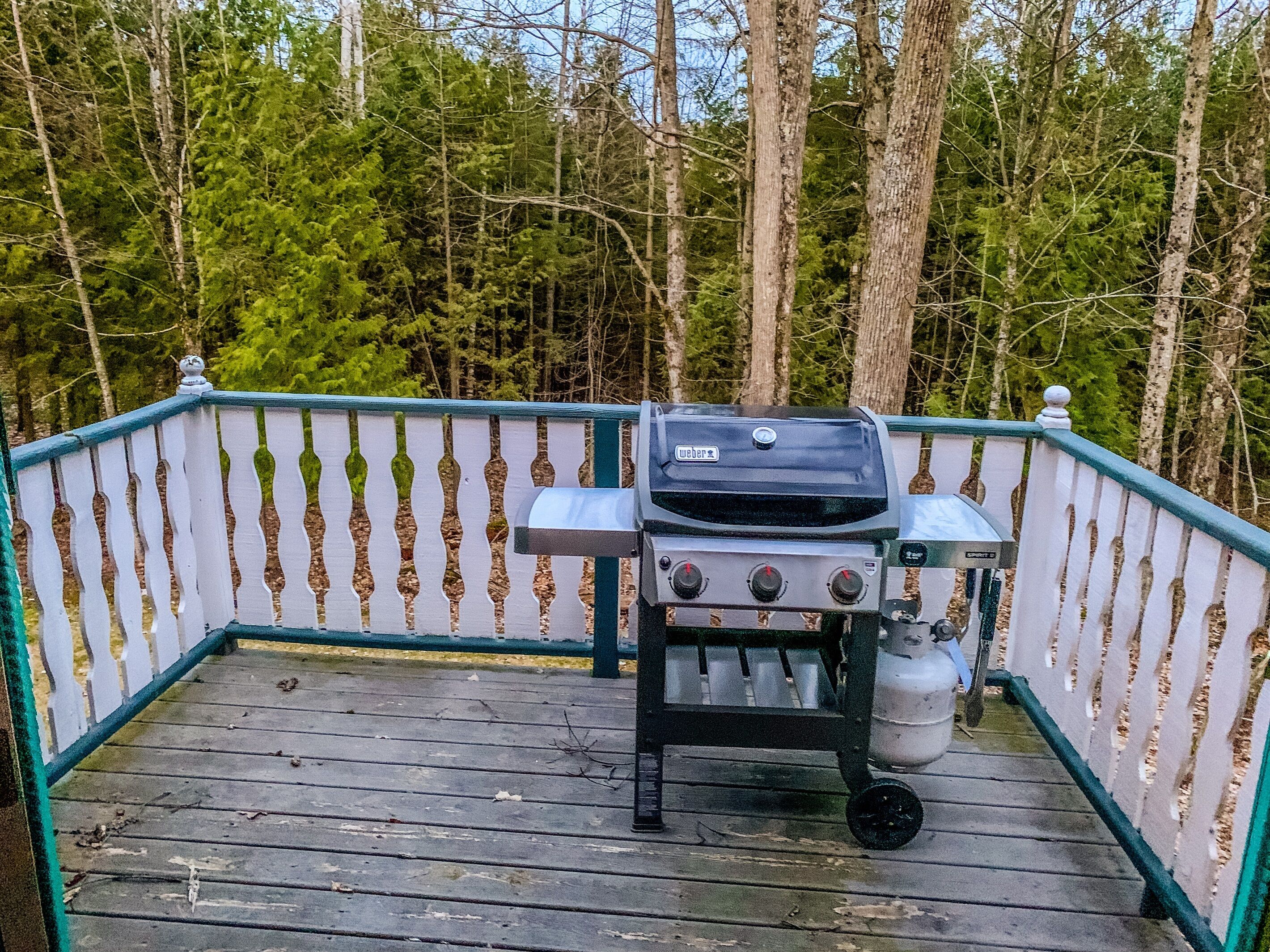 Un barbecue Weber portable sur une terrasse en bois, avec une clôture blanche faite de piquets.