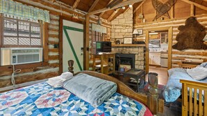 Una habitación rústica tipo cabaña de madera con una cama, chimenea, televisor y pared de piedra.
