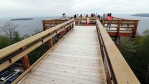 Una pasarela de madera con barandilla, con vistas a un cuerpo de agua y tierra a lo lejos.