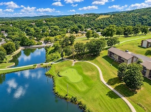Un parcours de golf avec un étang, entouré de bâtiments résidentiels et d’une végétation luxuriante.
