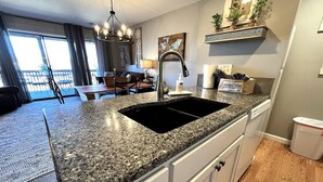 Eine Küche mit Granit-Arbeitsplatten, einem schwarzen Spülbecken, weißen Schränken und einem Essbereich mit Tisch und Stühlen.