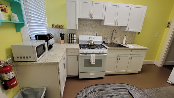 A compact kitchen with white cabinets, a stove, a microwave, and a sink.