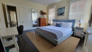 A bedroom with a bed, dresser, desk, chair, and a large mirror.
