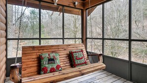 Eine Holzbank mit zwei Kissen, eine Holzbalkendecke und Blick auf Bäume durch große Fenster.
