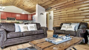 Ein gemütliches Wohnzimmer mit zwei braunen Ledersofas, einem Holztisch und einer Küche im Hintergrund.