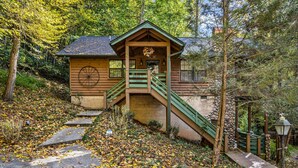 Eine Holzhütte mit einer Treppe, die zu einer Veranda führt, umgeben von Bäumen und Herbstlaub.