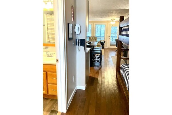 Un couloir au plancher de bois menant à une salle à manger équipée d’une table et de chaises.