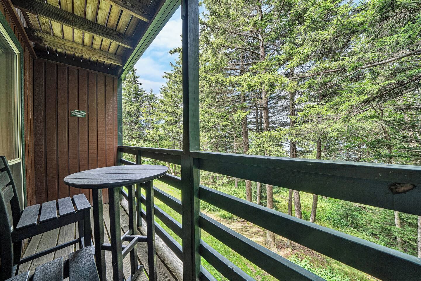 A wooden deck with a table and chairs, overlooking a forested area.