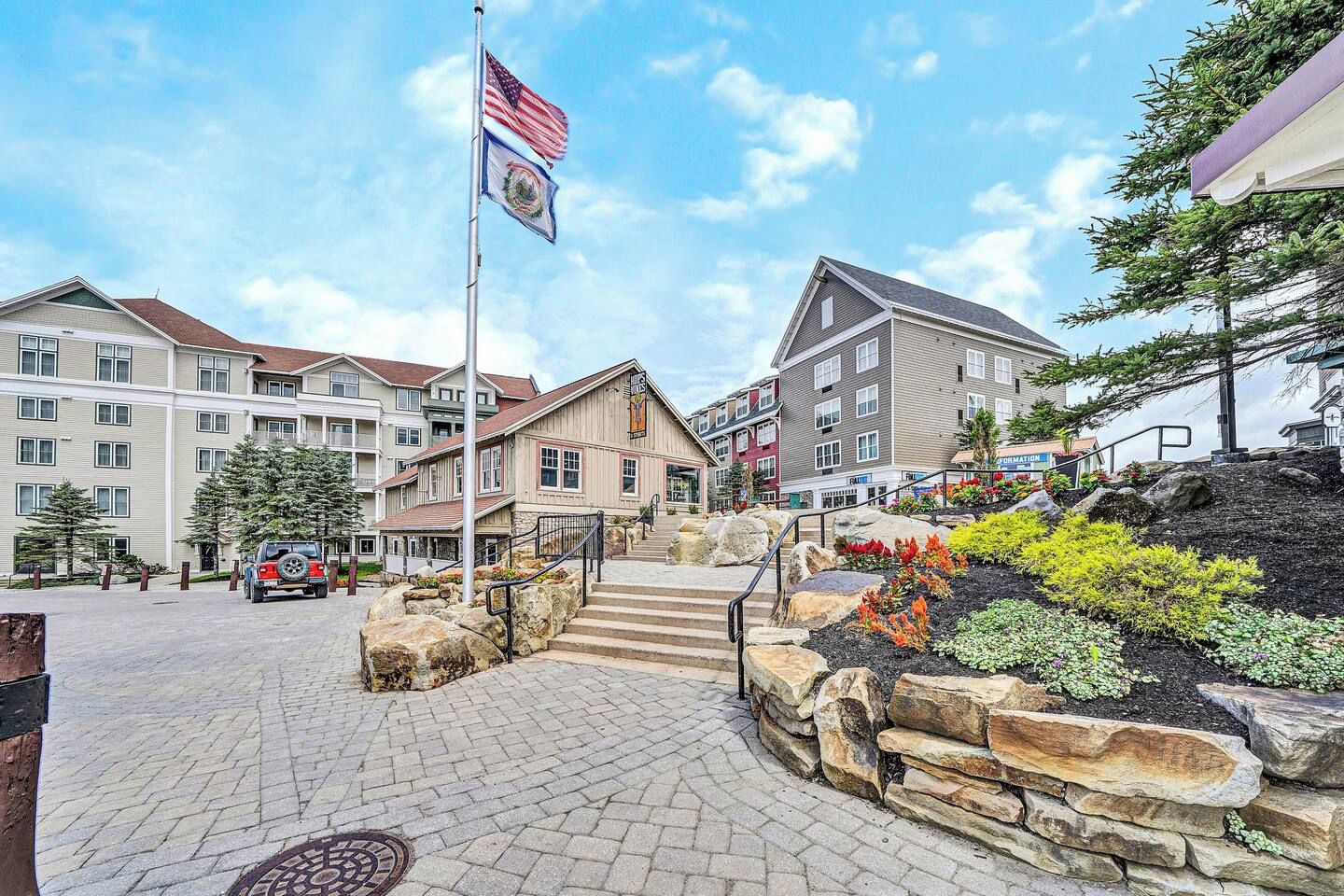 A hotel with a flagpole, stone steps, and a landscaped area with plants.