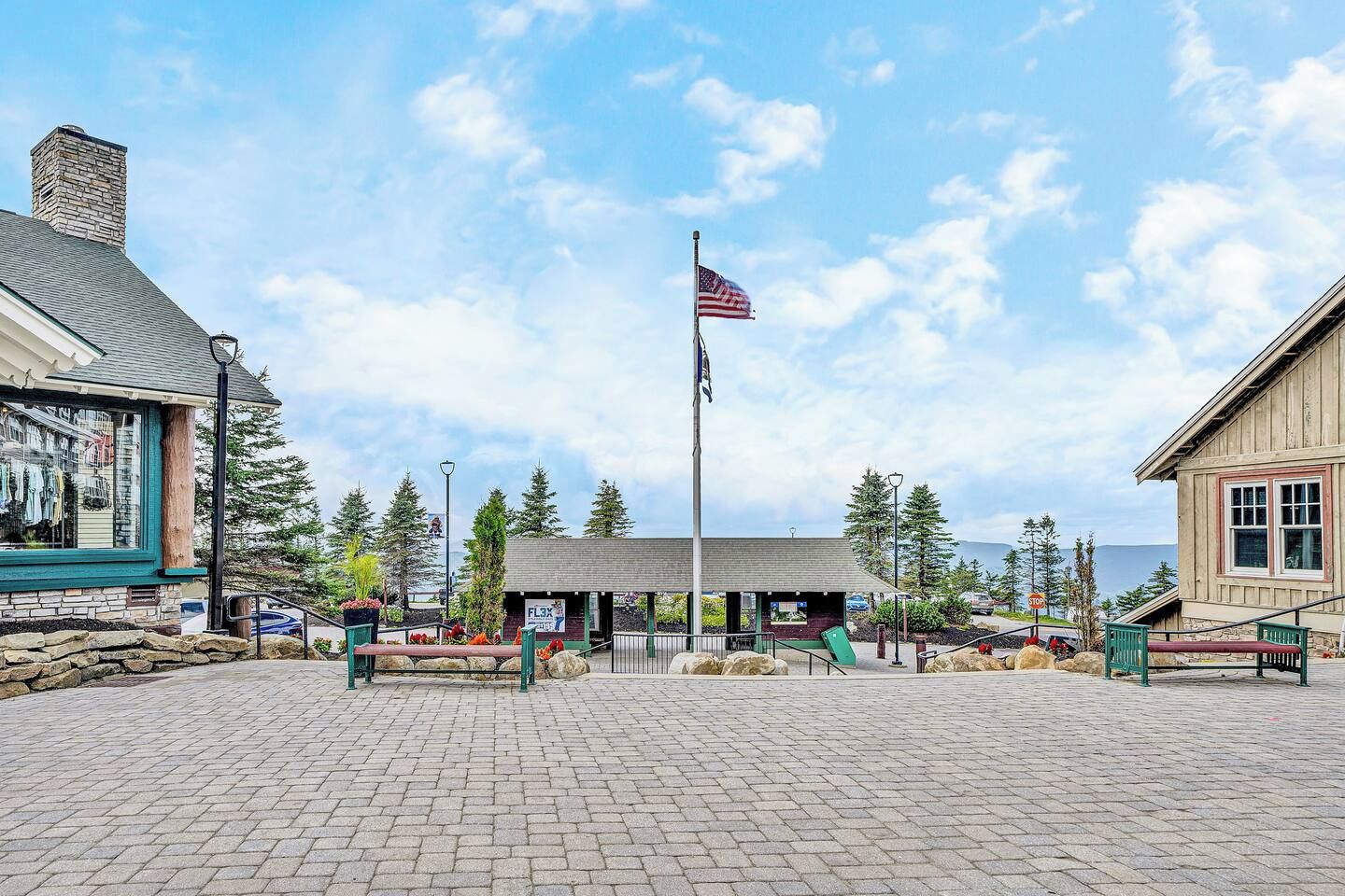 A paved plaza with a flagpole, a small building with a sign, and a wooden building with a window.