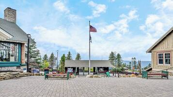A paved plaza with a flagpole, a small building with a sign, and a wooden building with a window.