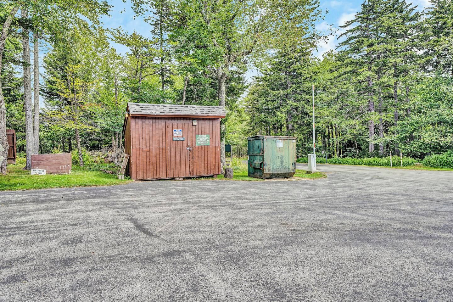 A gravel parking area with a small wooden structure and a green utility box.