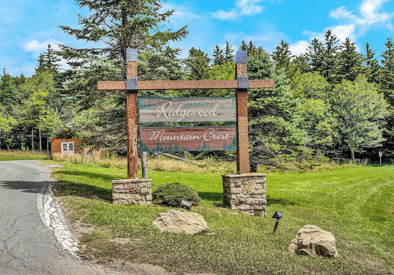 A wooden sign with the text 'Ridgewood Mountain Crest' in a rural setting with a road, trees, and a small building.