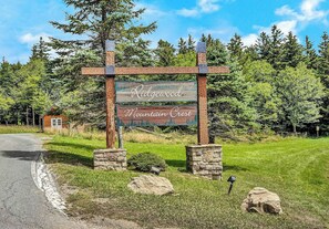 A wooden sign with the text 'Ridgewood Mountain Crest' in a rural setting with a road, trees, and a small building. - 23 Mountain Crest, Snowshoe, WV - Country Chic (Snowshoe)