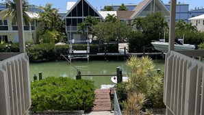 A view from a balcony overlooking a marina with boats docked, a clear sky, and buildings in the background. - BeachHouse @ Sombrero & Ocean access w/45’ Dock, kayaks and Bikes. (Marathon)