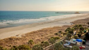 A beach with a pier extending into the sea, sandy dunes, and a fenced area with buildings. - Remodeled Studio-Ocnview-Steps2Beach-Kingston Plantation-Pool-Restaurant/Bar (Myrtle Beach)