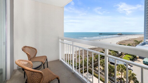 A balcony with wicker chairs, a white railing, and a view of the beach and ocean. - Remodeled Studio-Ocnview-Steps2Beach-Kingston Plantation-Pool-Restaurant/Bar (Myrtle Beach)