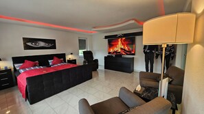 A modern bedroom with a large bed, a TV, a gaming chair, and a mannequin.