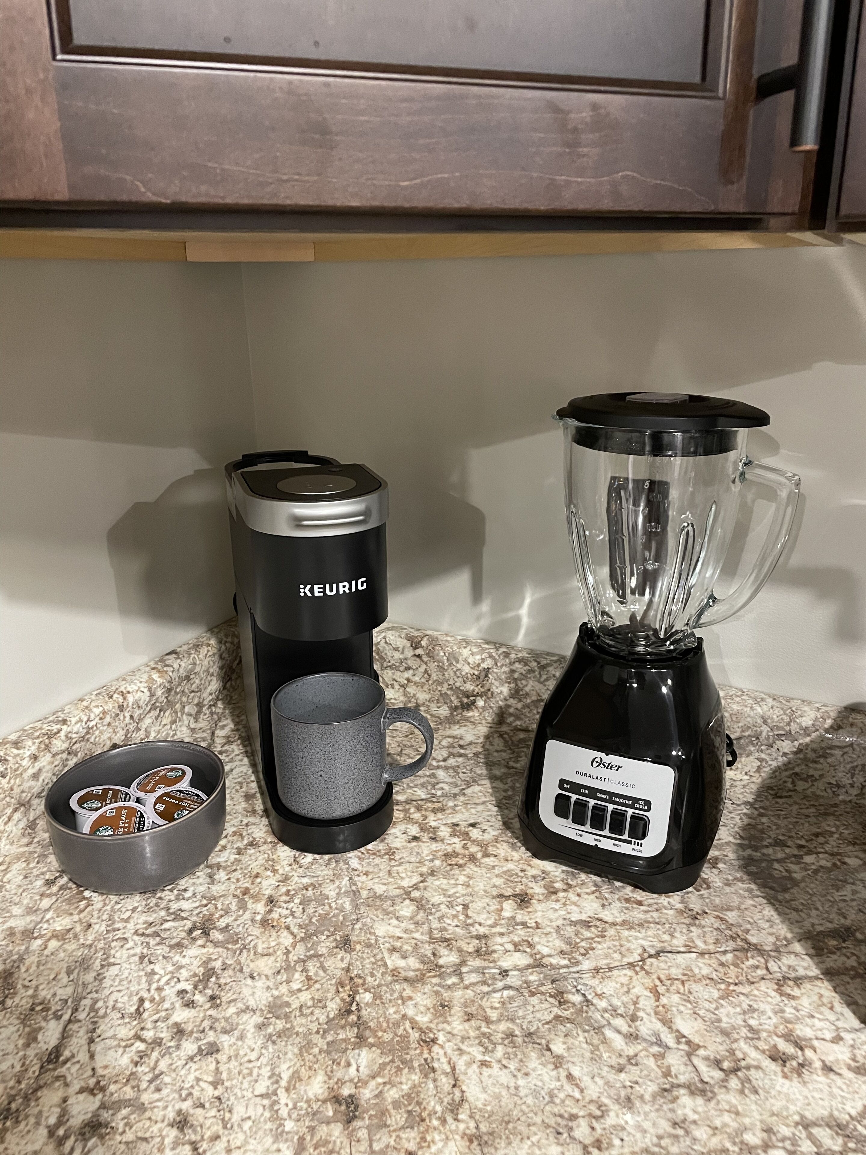 A kitchen counter with a Keurig coffee maker, a blender, and a bowl of coffee pods.