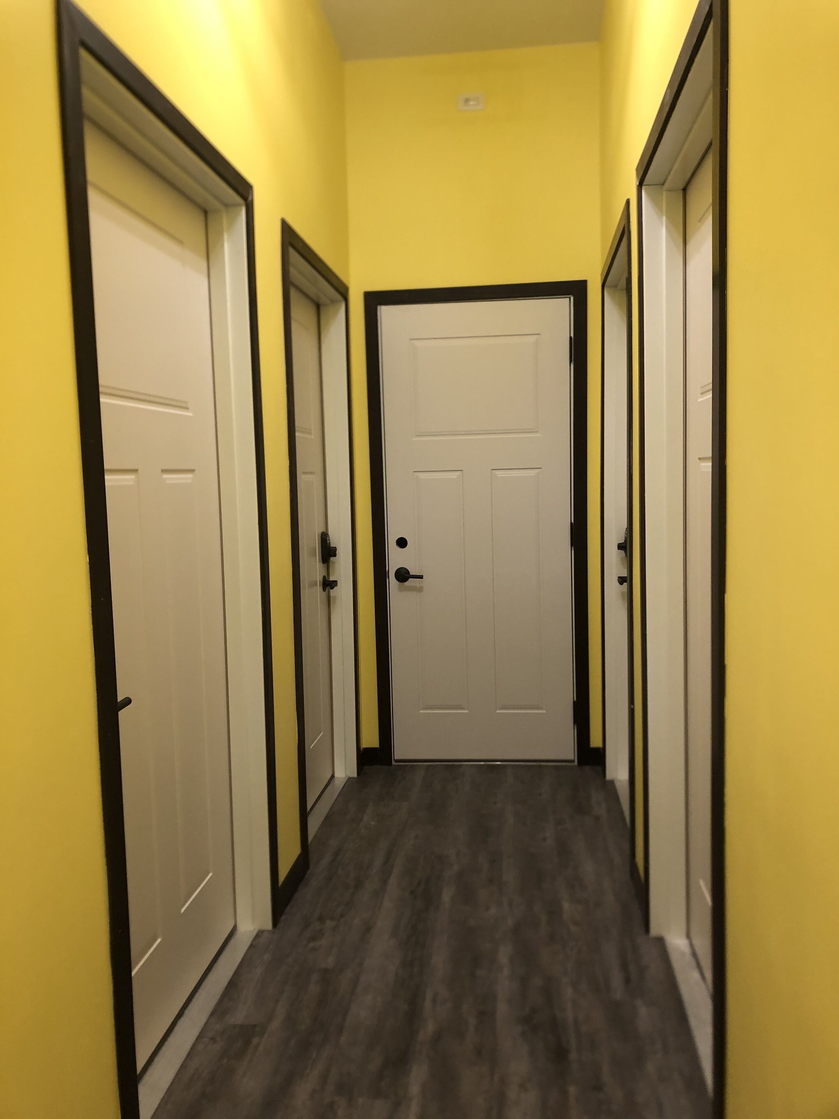 A hallway with yellow walls and dark flooring, leading to a white door with a black frame.