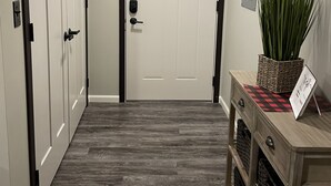 A hallway with a wooden floor, a white door, and a small wooden console table with a plant and a sign. - 1 of 3 NEW, NEW, NEW!  Downtown Wabasha Studio - Unit #100 113 Pembroke Ave. (Wabasha)
