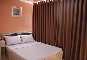 Una cama con ropa blanca, una mesita de noche con una lámpara y un cuadro en la pared.