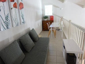 Un salon confortable avec un canapé gris, une table à manger avec des chaises et une rambarde blanche.