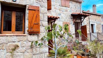 Un bâtiment en pierre avec des volets en bois, un petit porche et des plantes en pot.