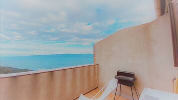Un balcon avec un barbecue, des chaises blanches et une vue sur la mer.