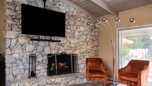 A stone fireplace with a TV mounted above it, two velvet armchairs, and a floor lamp. - Fully furnished Midcentury Home, 3 Bd/Den, Views, Best So PD Location (Palm Desert)