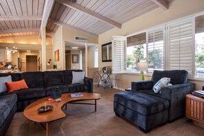 A spacious living area with a dark-colored sofa set, a wooden coffee table, and a window with white shutters.