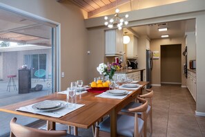 A dining area with a wooden table set for four, a vase of flowers, and a fruit bowl.